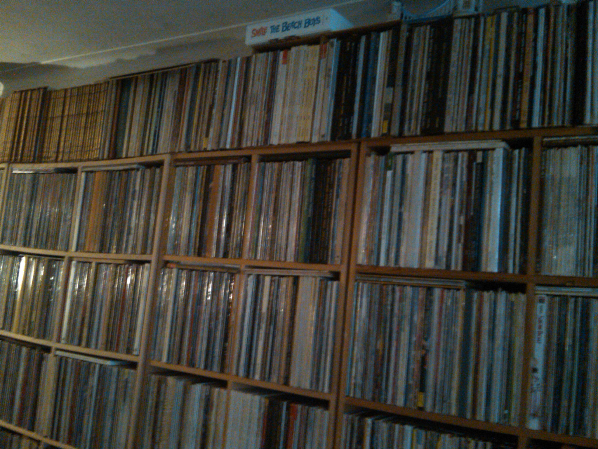 A wall of vinyl LPs with the Smile Sessions box lying horizontally on top of it.