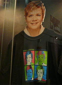 a cardboard cutout of Alsop in a display case wearing a commemorative t-shirt featuring four more Alsops