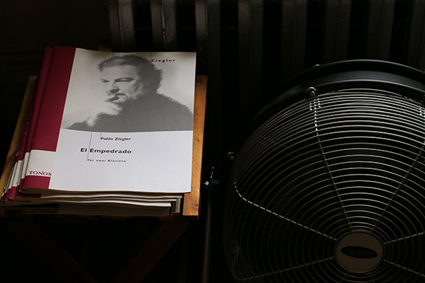 A pile of Ziegler's published scores lies on the floor in his apartment next to a fan. 