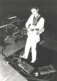 Dresher in white suit playing electric guitar and operating a variety of foot pedals.