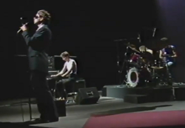 Eckert wearing sunglasses and singing into a micropphone, Dresher playing synthesizer keyboard and Reffkin playing drum-kit