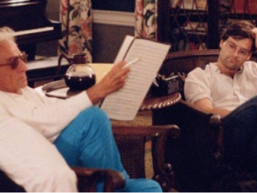 Leonard Bernstein holding a cigarette and studying a score as Daron Hagen looks on.