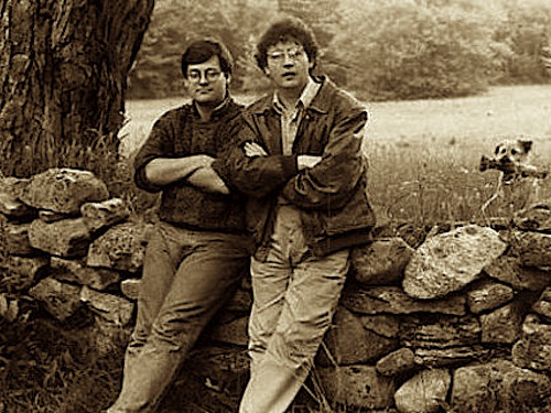 Daron Hagen and Paul Muldoon leaning against a stone fence in the countryside.