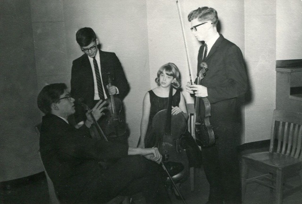 Historic B&W photo of Jacovin Quartet members holding their instruments and talking.