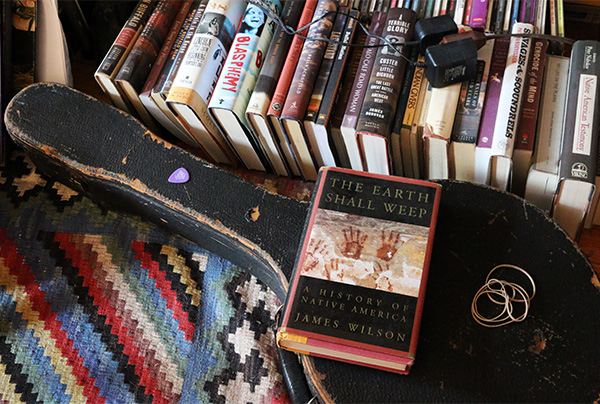 A pile of books on the floor, one (The Earth Shall Weep - A History of Native America) on top of a banjo case