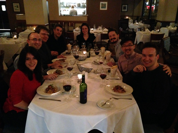 The seven composers featured at the institute with Kevin Puts around a dining table at a restaurant eating and drinking red wine.
