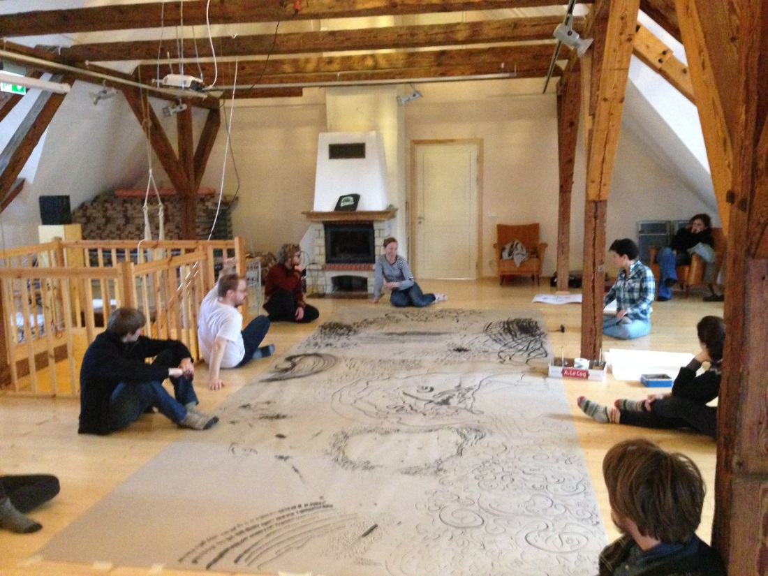 A group of people sitting on the floor around a very large nhandwritten manuscript