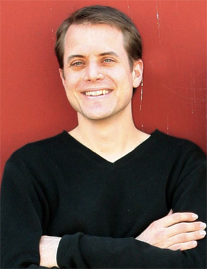 Bradley Colten in a black shirt smiling against a red background.