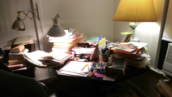An extremely cluttered desk filled with various manuscripts and folders.