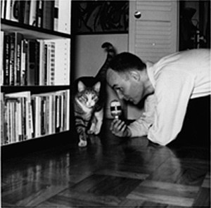 Dockstader on floor near bookcase holding a microphone near a cat walking by