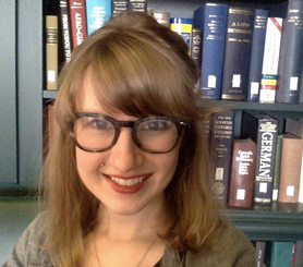 Caitlin Schmid, wearing glasses, sitting in front of a bookcase filled with books