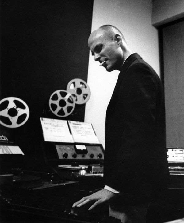 Dockstader working at a reel-toreel tape console standing up and smoking a cigarette