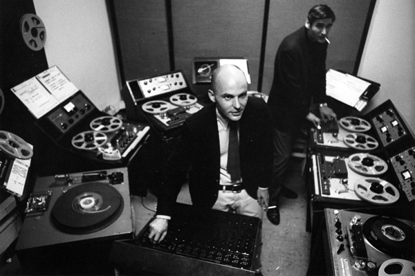 Jim Reichert standing in back operating one of many reel-to-reel tape machines and Tod Dockstader sitting in front of a console turning a knob.