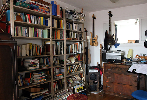 Shelves crammed full of books and various electric guitars hanging on a wall