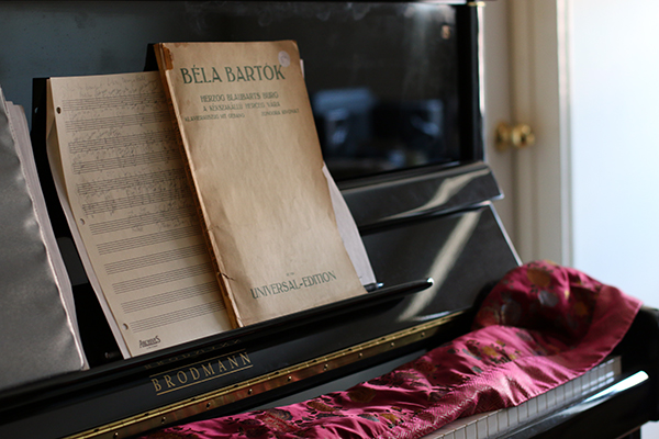 A page of handwritten manuscript and a Bartók score published by Universal Edition are side by side in front of a Boradman upright piano