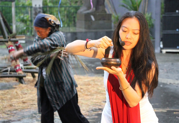 Jen Shyu singing and ribbing a brass bowl in an outdoor ceremony .