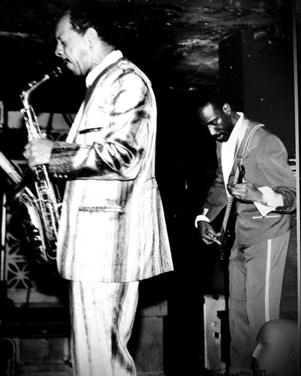 Ornette Coleman playing saxophone and Jamaaladeen Tacuma playing bass on stage in performance.