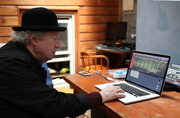 A Bowler-hat clad Morrow sits at a desk and triggers sound from his laptop.