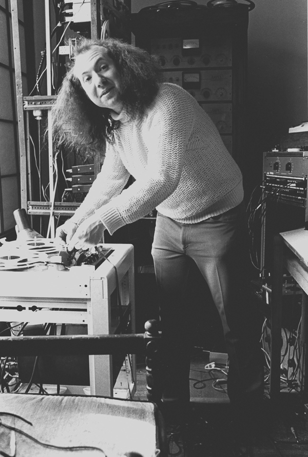 A long-haired Charlie Morrow leaning at a table and surrounded by a lot of electronic equipment