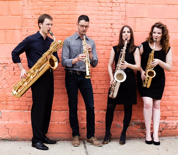 The members of the New Thread Quartet playing their saxophones against a wall.