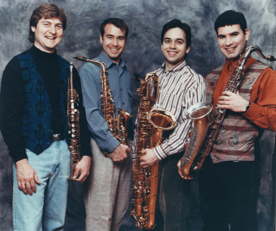The four 1995-2001 PRISM members holding their instruments and standing in front of an abstract painting