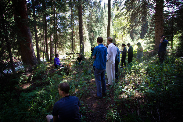 A performance happening outdoors in the middle of a forest with audience members standing and listening.