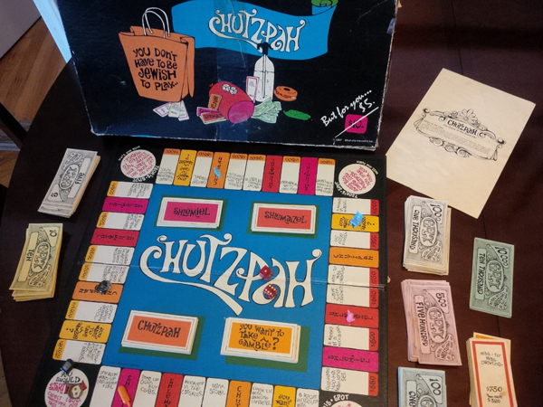 A photo of the boardgame chutzpah showing the playing board, sets of cards, money, and the cover of the box it was sold in.