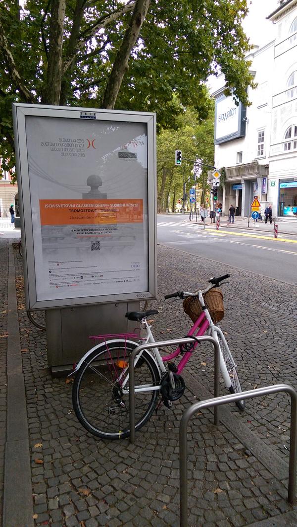 A bicycle parked in front of a poster for the 2015 ISCM World Music Days on a street in Ljubljana.