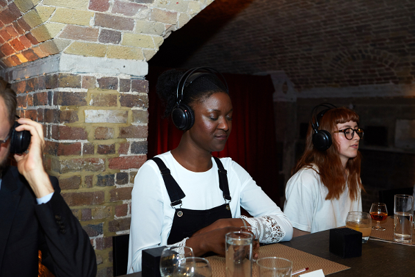 Three people at a table wearing headphones and sipping whisky