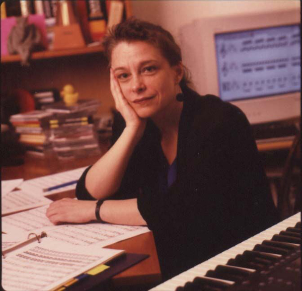 Mary Jane Leach at her work desk with manuscripts, an electric keyboard and a computer monitor in the background.