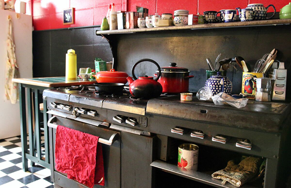 A couple of pots and a tea kettle sit on top of a stove, various containers and other kitchen paraphernalia are to the right of it and on a shelf above it.