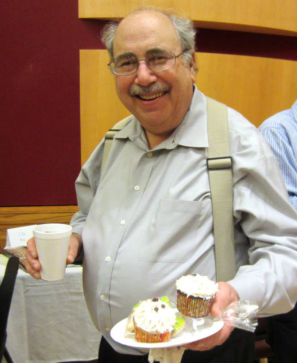 David Stock wearing suspenders and smiling as he holds a plate with a couple of cupcakes.