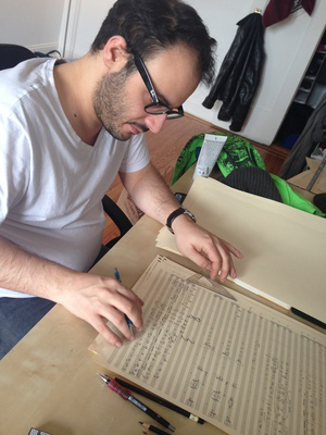 Vincent Calianno sitting at a desk and staring at a large orchestral score manuscript.