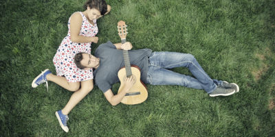 Young man playing guitar to his girlfriend in nature - dating couple