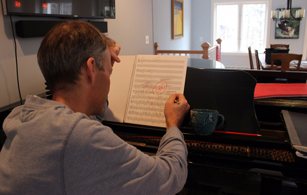 Jim Stephenson sitting in front of his piano, struggling in front of a piece of score paper that is marked up with various things crossed out and a section labelled "Bad"
