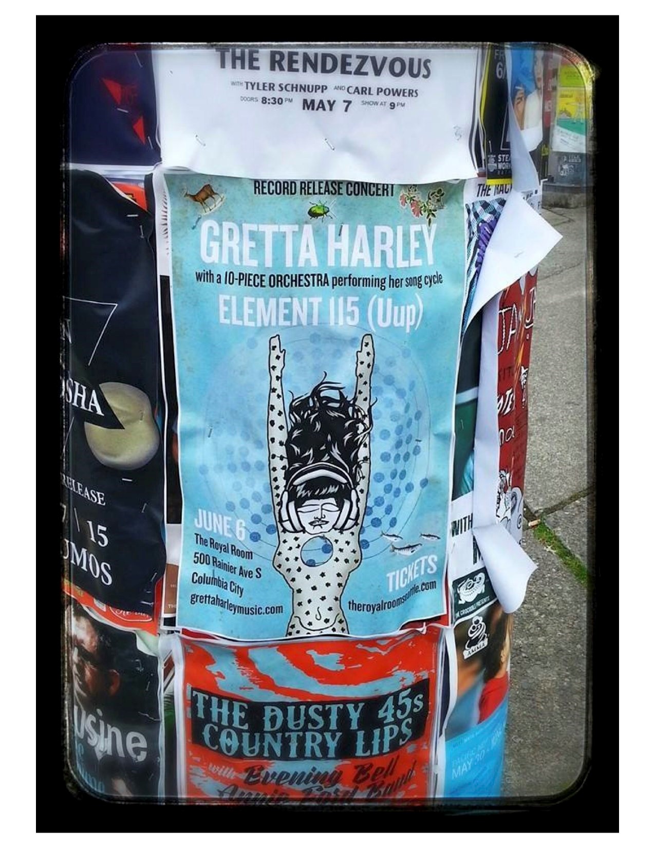 A concert poster for the 10-piece ensemble live concert of Gretta Harley's Elenet 115 on a pole with other concert posters.