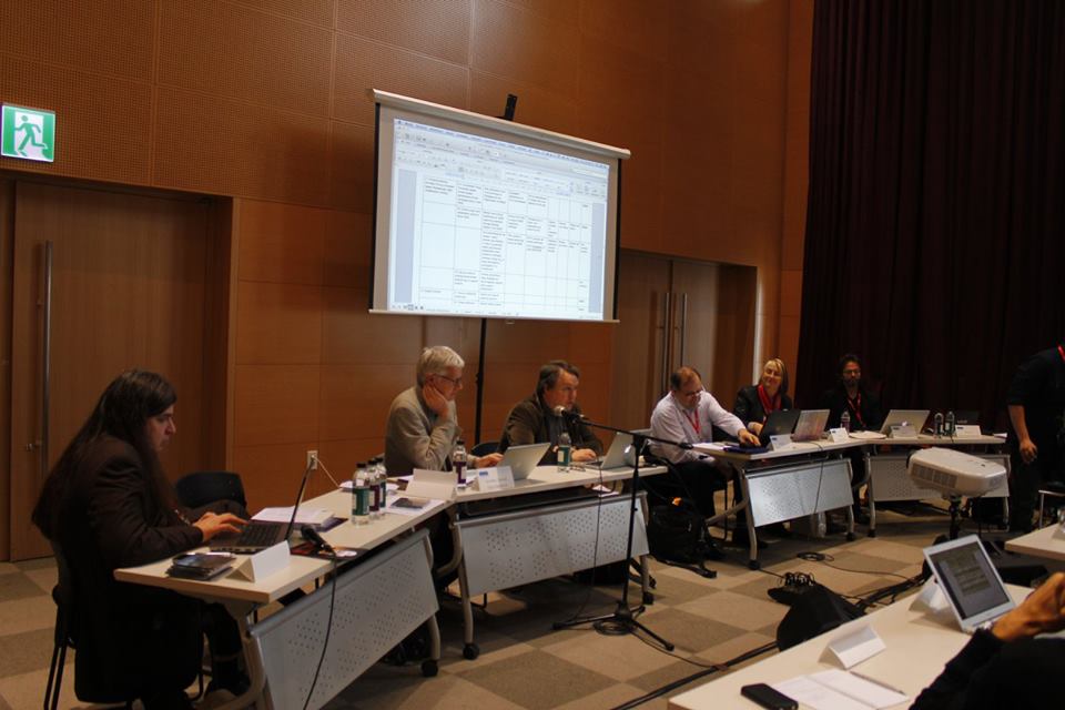 FJO seated at a series of desks along with other members of the ISCM Executive Committee, with a screen projection in back of them.