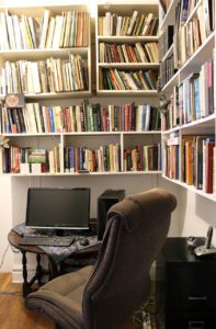 Wall to wall bookshelves surround a work station with a laptop and a chair.