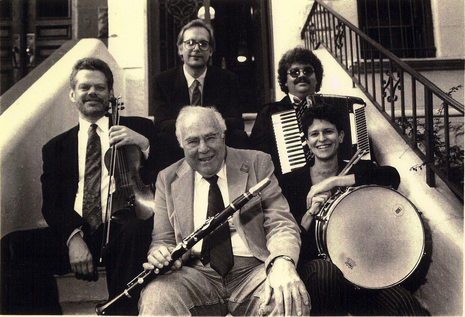 Photo of Michael Hess (holding violin), Howie Leess (holding clarinet), Michael Hess, smail Butera (holding accordion), and Eve Sicular (holding a snare drum)