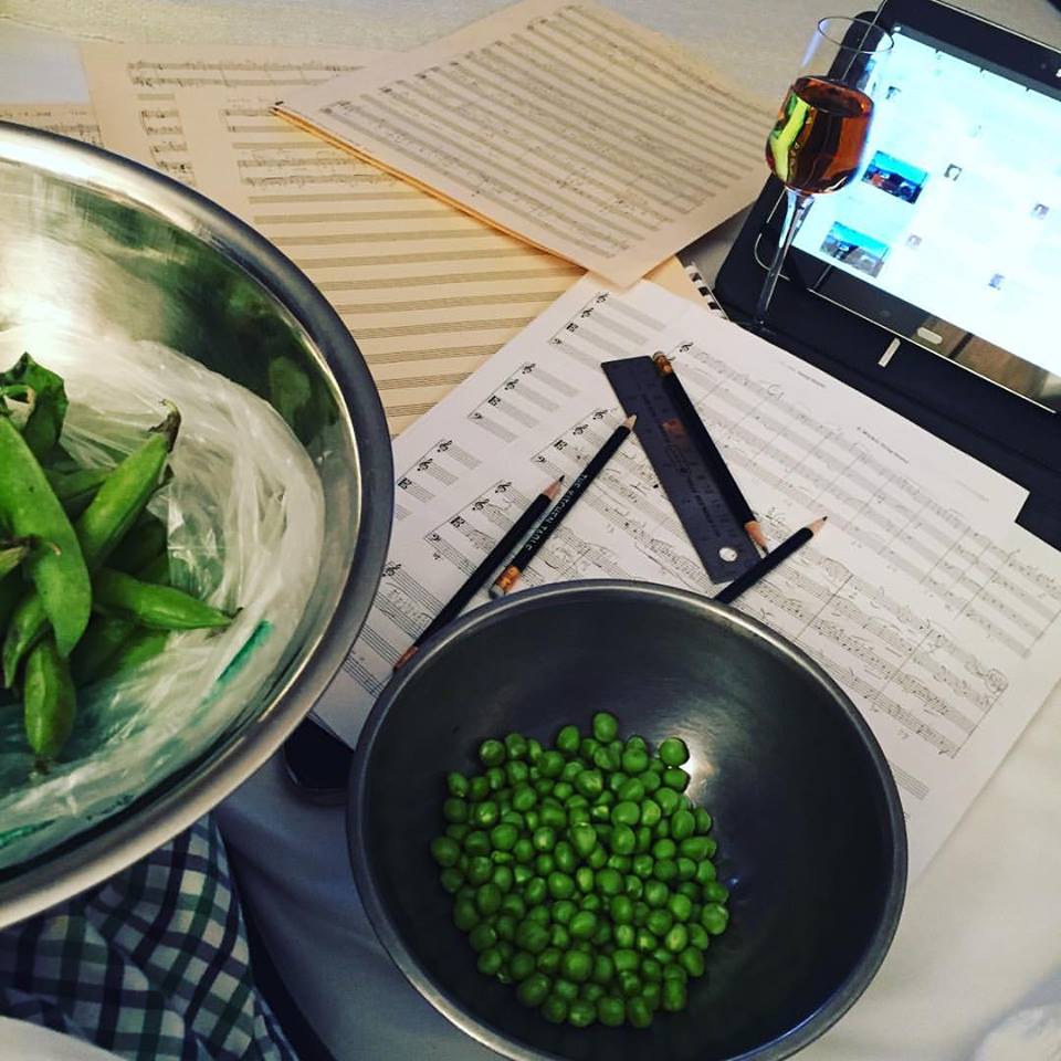 Ed Windels's table in the midst of shelling peas (with bowls of shelled and unshelled peas), writing a string quartet (with manuscript paper, ruler, and writing implements), drinking a glass of wine, and a computer monitor.