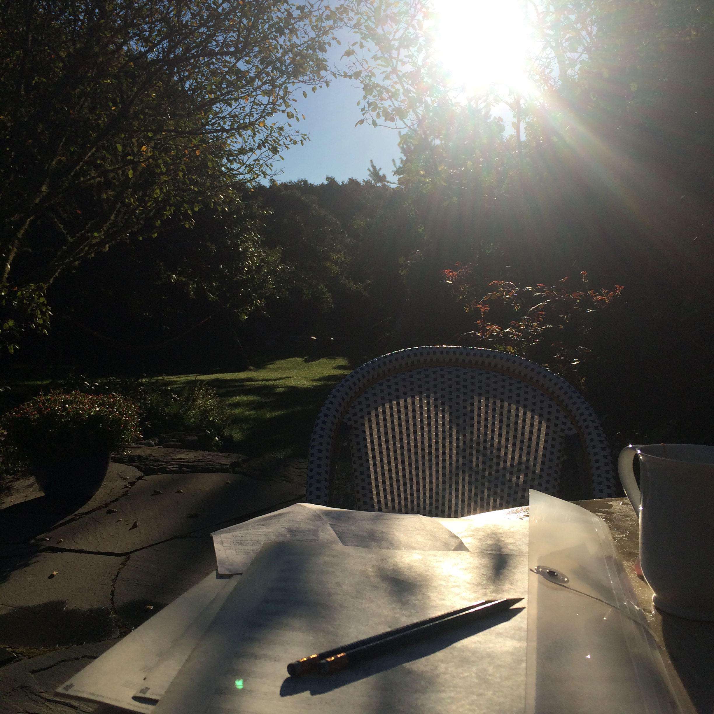 A pen sits atop a blank page of music notation paper on a table outside, the sun setting in the background.