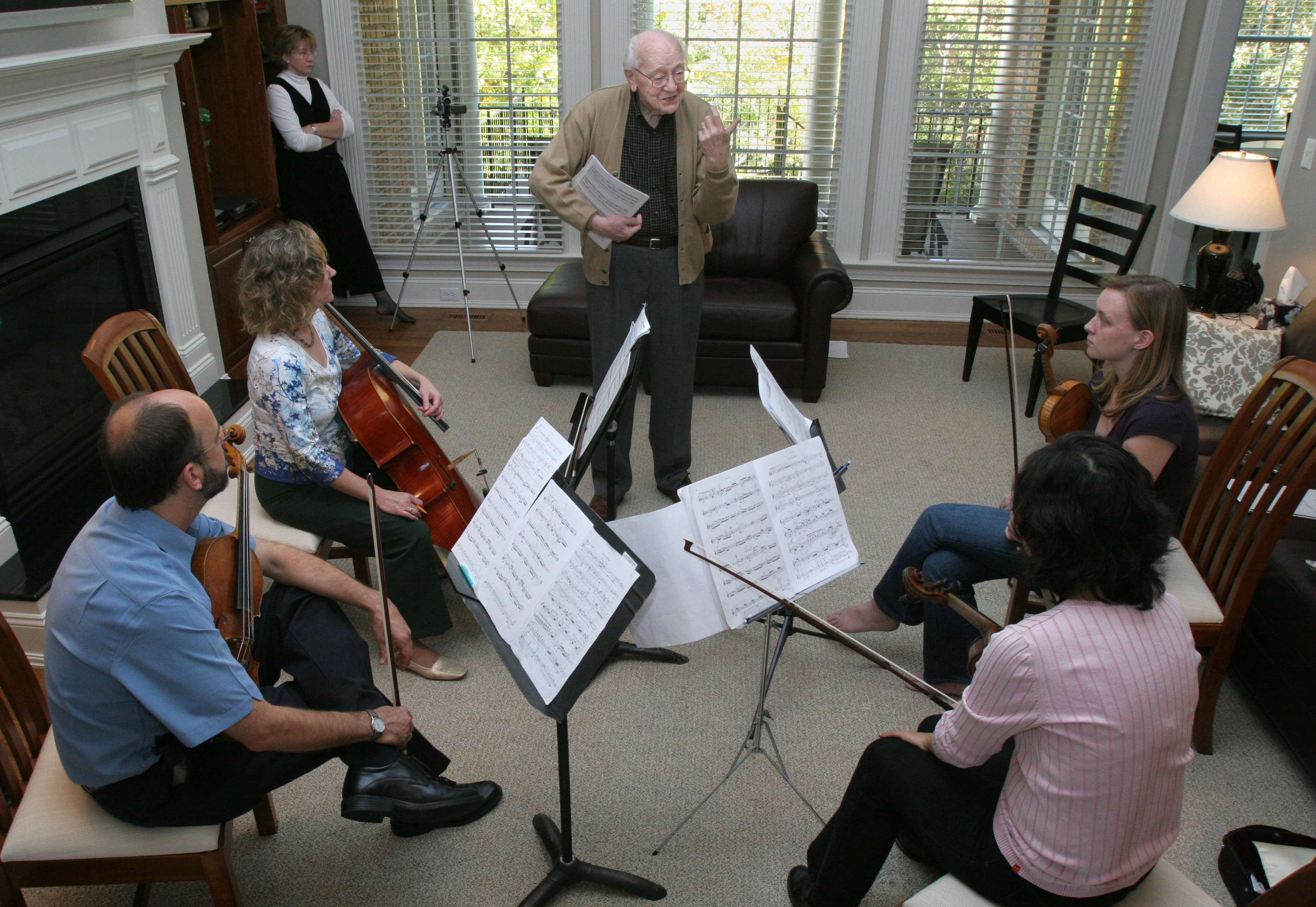 Karel Husa standing surrounded by a string quartet rehearsing in his home.