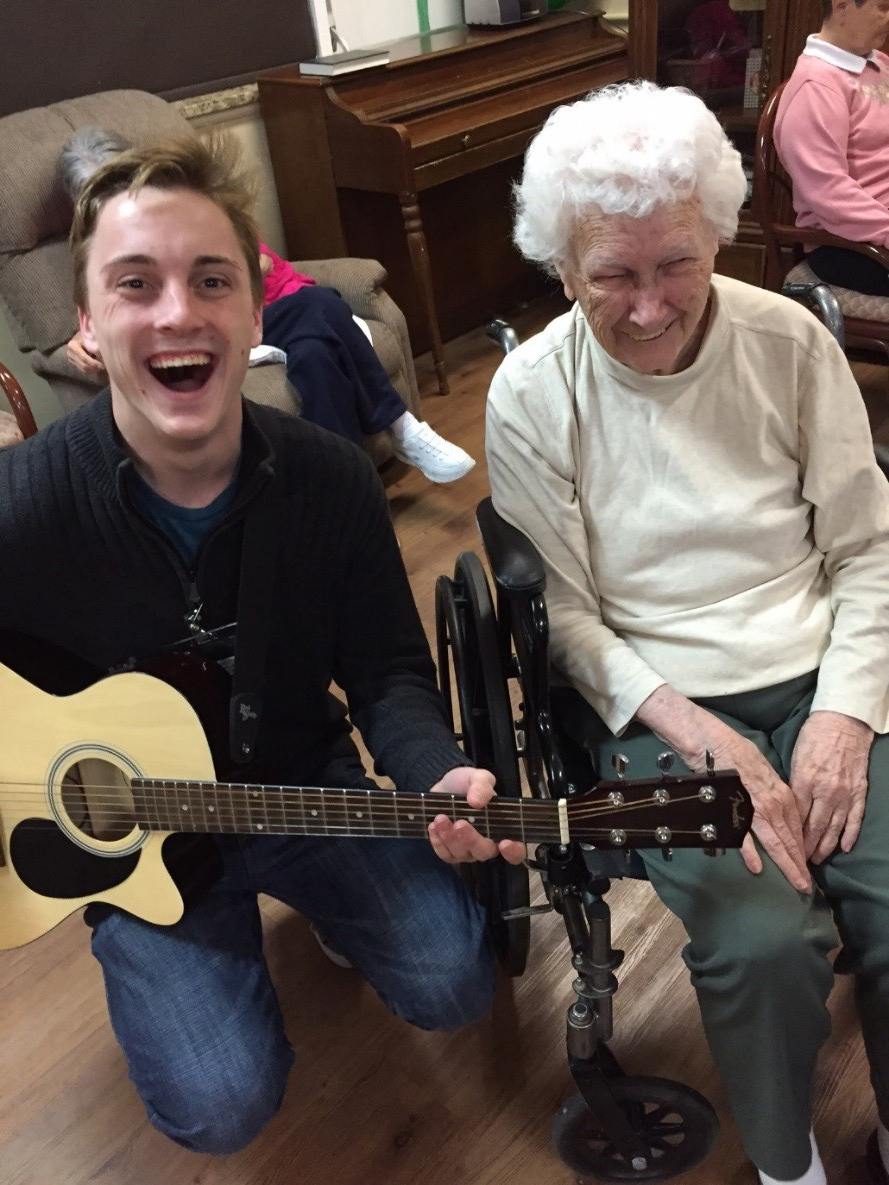 Yoder sitting with a guitar next to one of the retirement center residents.