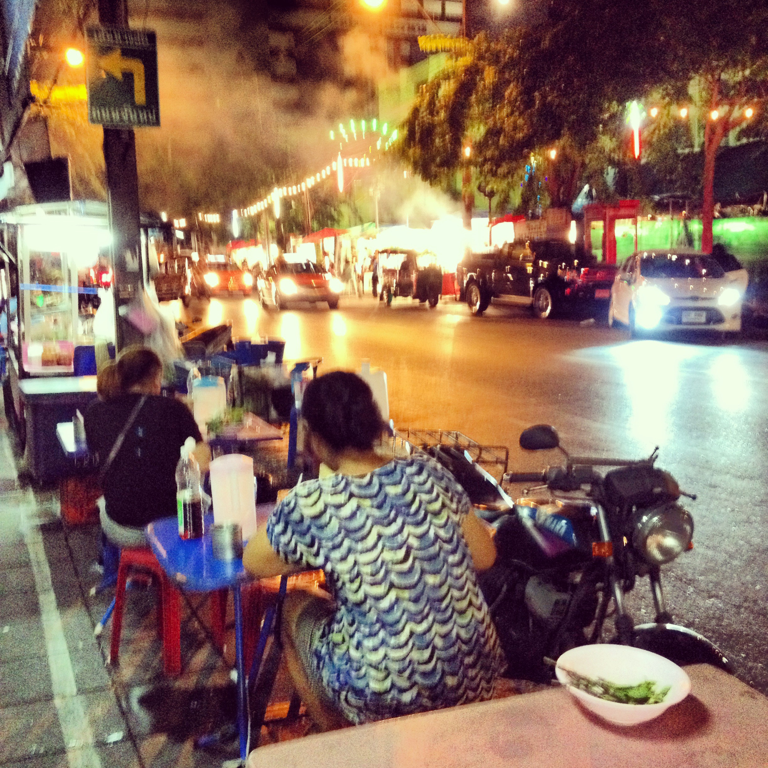 People eating at tables outside on a street in Bangkok.