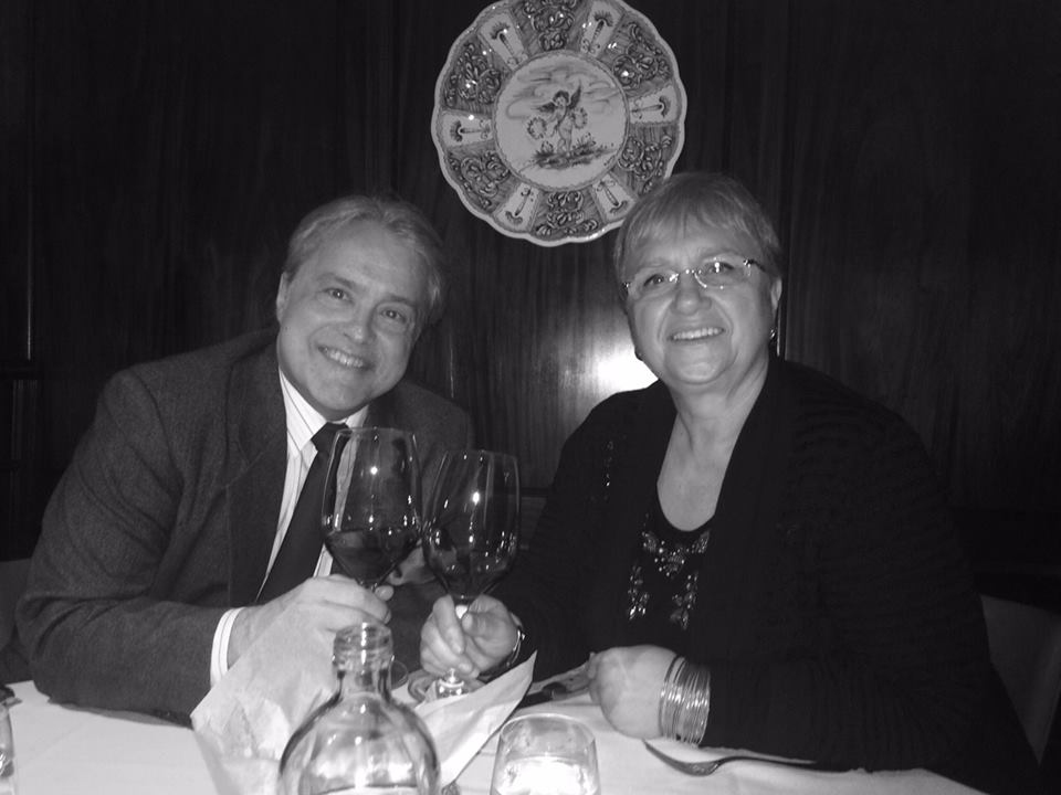 Daniel Brewbaker and Lidia Bastianich holding glasses of red wine at a dinner table.