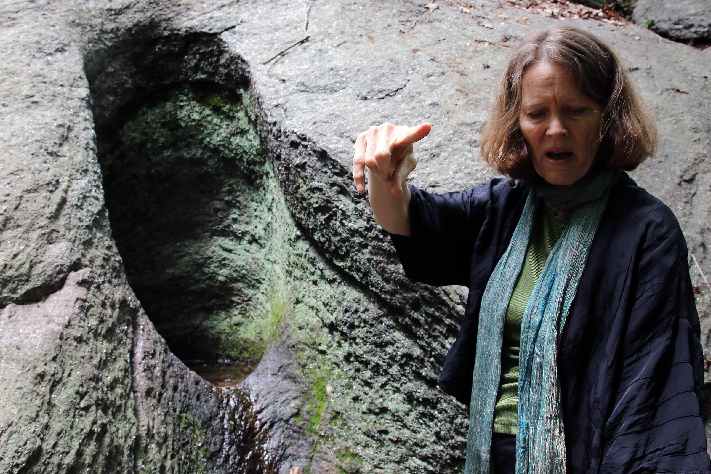 Kristin Norderval standing beside a prehistoric glacial drill hole in Inwood Hill Park