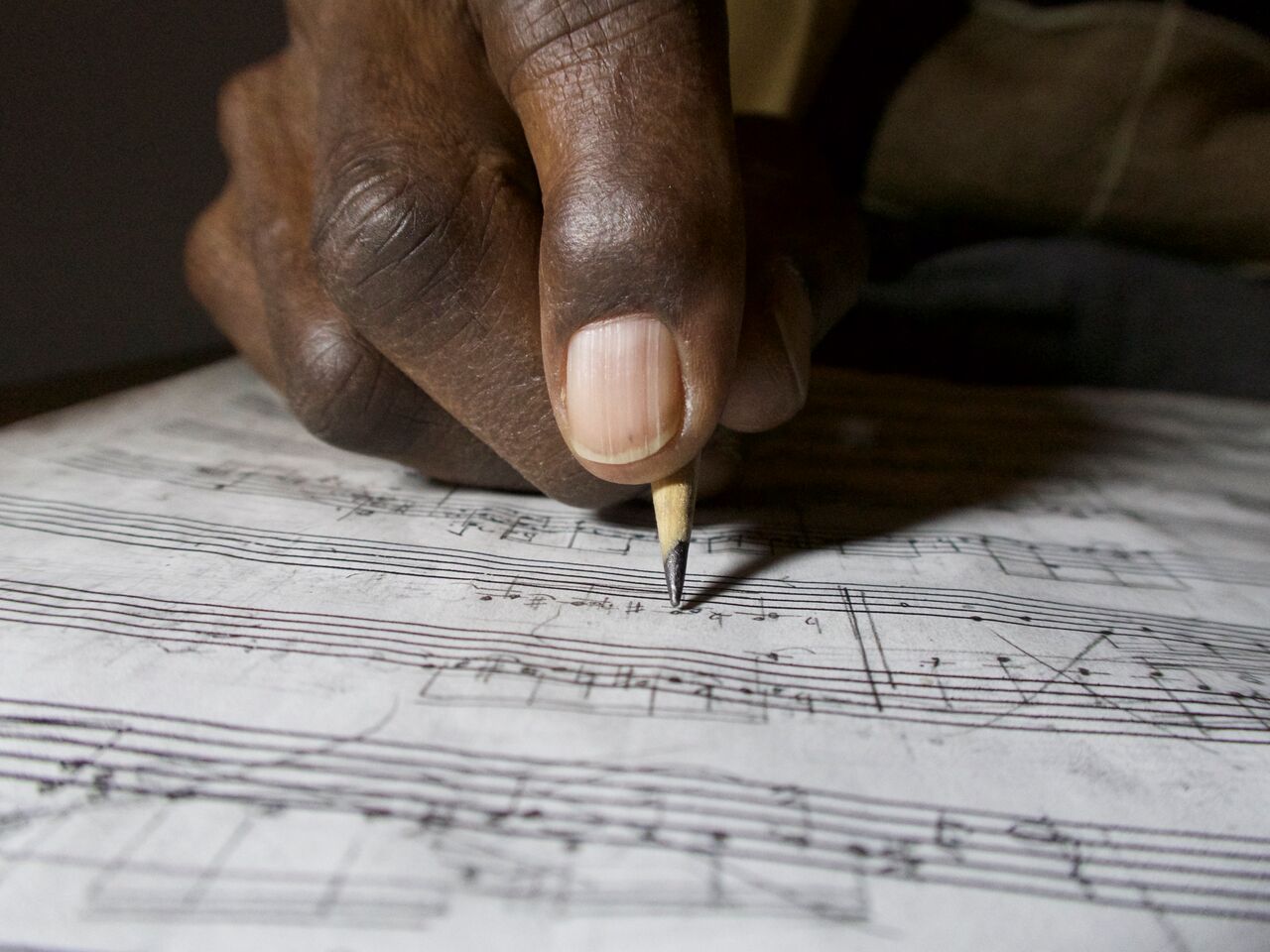 George Walker's hand holding a pencil and writing on a page of music notation paper.