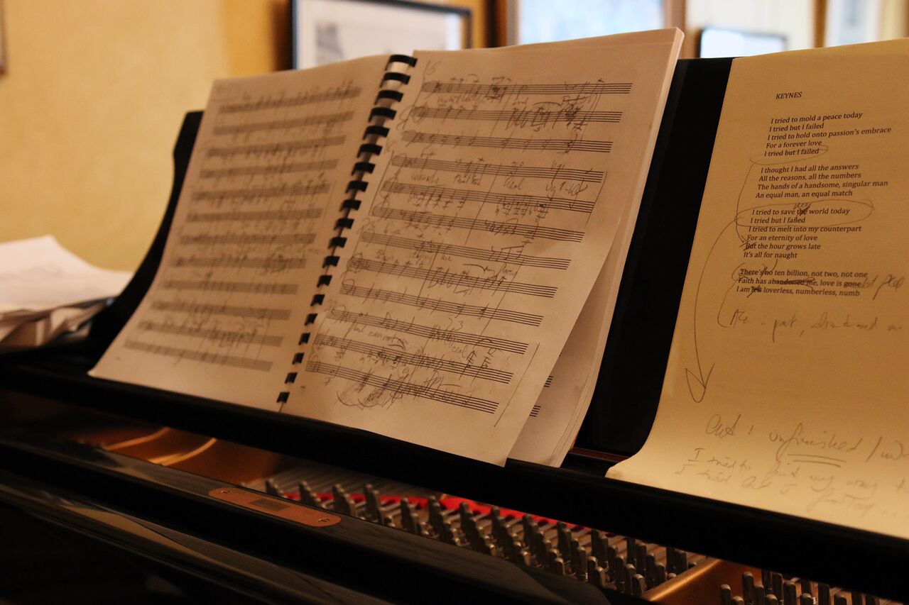A manuscript for a vocal setting by Stefania de Kenessey sits on top of her piano next to a sheet with the text she is setting.
