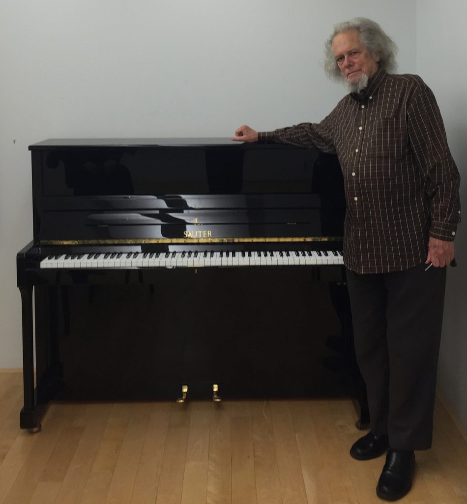 Bruce Mather standing beside an upright piano that has been retuned to 96-tone equal temperament (the Carrillo piano).