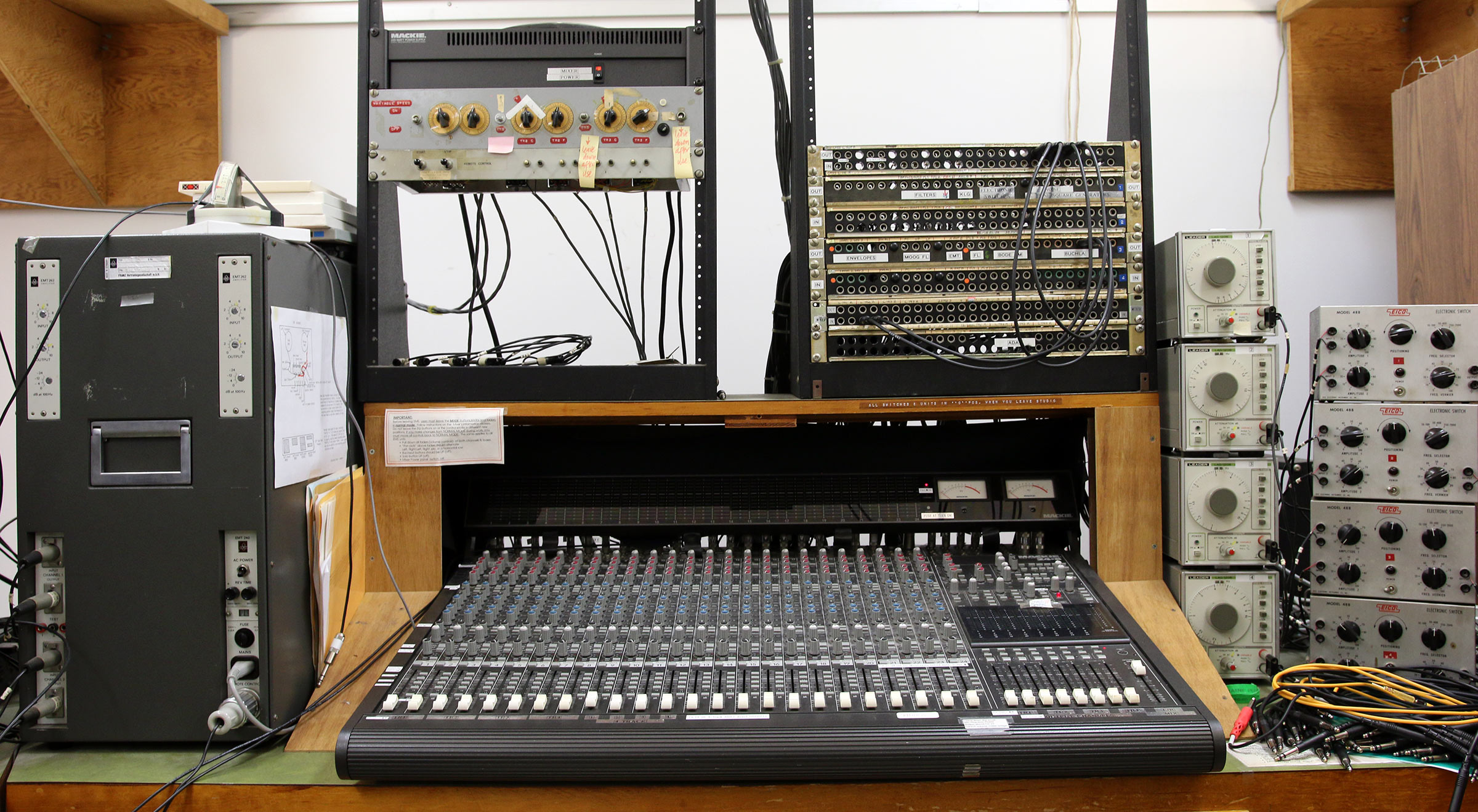 Various vintage oscillators and reverb units surround a state of the art digital mixing console.